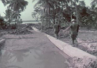 Screenshot from corrected film of two men walking on a pipe at the Dong Tam Base Camp Construction.